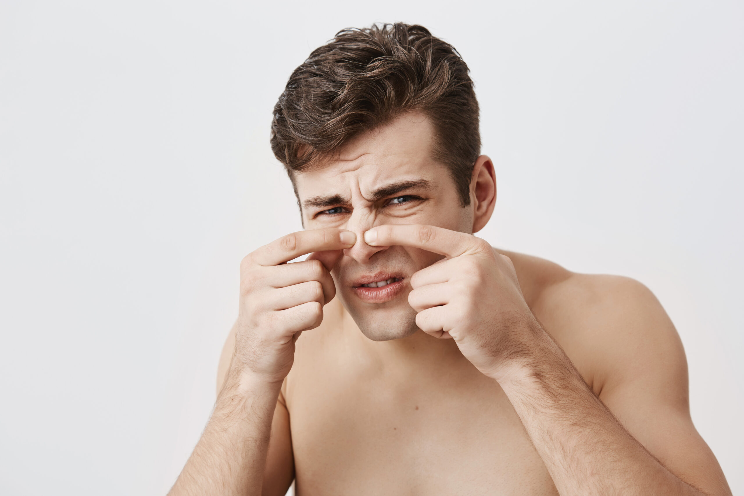 Naked muscular male with appealing appearance, frowning face, touching nose, having skin problems. Caucasian man with dark hair, looking at camera with his blue eyes. Beauty and youth concept.